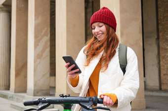 红色头发的人女孩旅游背包移动电话租金e-scooter街道欧洲城市