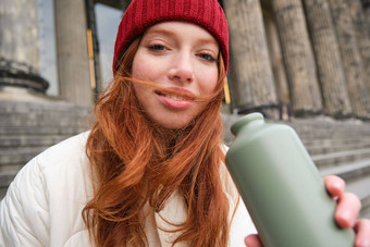 肖像红色头发的人女人喝热水瓶坐着街楼梯享受热喝瓶