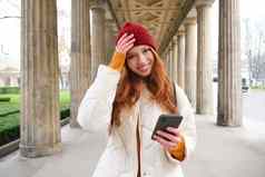 快乐年轻的女模型站街持有移动电话智能手机应用程序路线在线地图