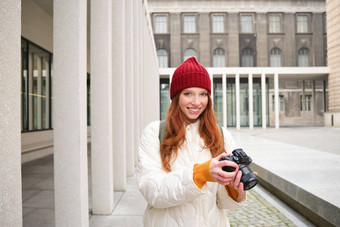 微笑红色头发的人女孩摄影师采取图片城市使照片在户外专业相机