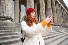 肖像年轻的博主红色头发的人女孩旅游需要图片观光使照片智能手机相机记录视频微笑