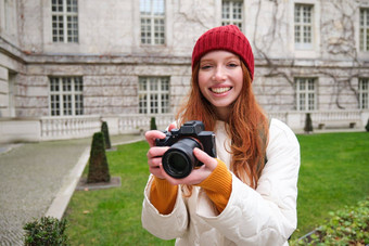 红色头发的人女孩摄影师需要照片专业相机在户外捕捉streetstyle照片兴奋采取图片