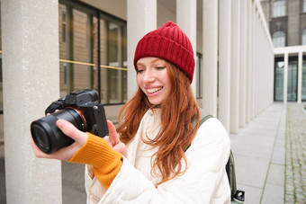 美丽的瑞德女孩摄影师专业相机需要图片在户外走城市采取照片观光