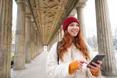 快乐年轻的女模型站街持有移动电话智能手机应用程序路线在线地图