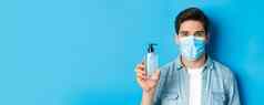 概念冠状病毒流感大流行预防措施特写镜头年轻的男人。医疗面具建议手洗手液显示防腐剂瓶站蓝色的背景