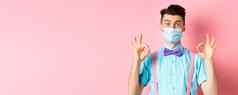 冠状病毒医疗保健检疫概念快乐的家伙医疗面具节日蝴蝶结显示好手势使迹象微笑相机粉红色的背景