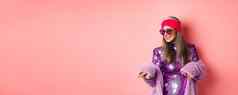 时尚亚洲高级女人跳舞迪斯科穿闪闪发光的闪亮的衣服心形的太阳镜有趣的站粉红色的背景