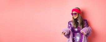 时尚亚洲高级女人跳舞迪斯科穿闪闪发光的闪亮的衣服心形的太阳镜有趣的站粉红色的背景