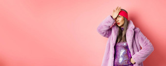 时尚购物概念生气高级女人卷眼睛使facepalm指蹩脚的站时尚的紫色的冬天外套闪闪发光的衣服粉红色的背景