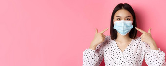 科维德流感大流行生活方式概念卡哇伊亚洲女孩指出手指脸面具穿预防措施冠状病毒微笑眼睛粉红色的背景