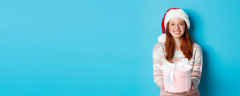 冬天庆祝活动概念美丽的红色头发的人女孩圣诞老人他祝快乐圣诞节给礼物微笑站蓝色的背景