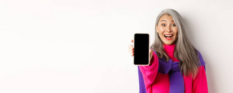 在线购物关闭时尚的亚洲高级女人扩展手移动电话显示空白智能手机屏幕微笑站白色背景