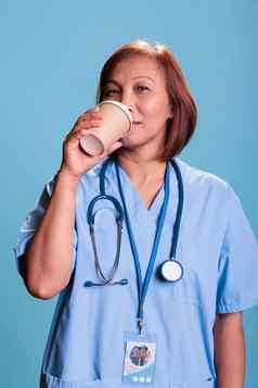 高级亚洲护士持有饮料杯喝咖啡检查访问