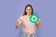 漂亮的乐观女人显示绿色回收标志持有塑料瓶手