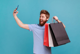 男人。蓝色的t恤持有购物袋会说话的自拍智能手机满意购买