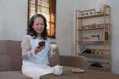 快乐的退休亚洲女人移动电话闲谈，聊天孙子放松生活房间