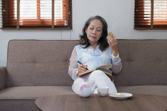 肖像华丽的岁的亚洲女人休闲衣服吃饼干写作日记放松生活房间