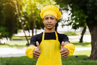 黑色的非洲少年烹饪显示拇指厨师他黄色的围裙统一的烹饪面团面包店有创意的广告咖啡馆餐厅