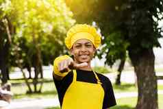 英俊的非洲少年烹饪点黑色的孩子烹饪厨师他黄色的围裙统一的微笑指出户外有创意的广告咖啡馆餐厅