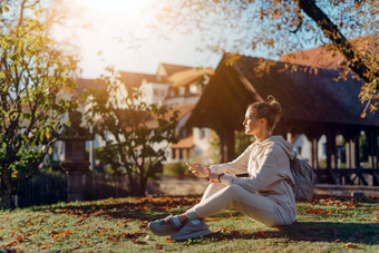 年轻的时尚十几岁的女孩智能手机europian公园秋天坐着微笑时尚的年轻的女人秋天公园发短信处理过充满活力的颜色美丽的金发女郎十几岁的女孩穿休闲现代秋天装坐着公园秋天处理过充满活力的颜色褐色音调