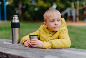 男孩坐着木表格热水瓶杯茶距离男孩坐在表格公园秋天季节孩子男孩儿子秋天公园坐着木板凳上表格孩子在户外