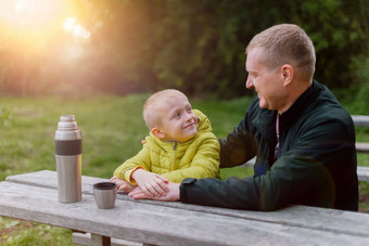 快乐家庭父亲孩子男孩儿子玩笑秋天公园坐着木板凳上表格父亲孩子有趣的在户外玩父亲儿子坐着板凳上会说话的热水瓶