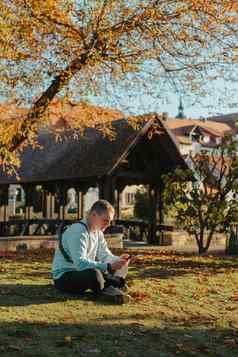 专业摄影师采取图片美丽的秋天公园男人。专业摄影师坐相机智能手机秋天公园处理过充满活力的颜色褐色音调