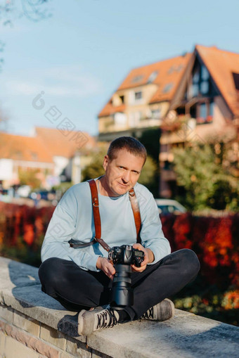 男人。坐着欧洲城市持有照片相机当代时尚的博主摄影师英俊的男人。采取自拍旅行欧洲
