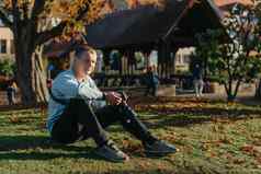 专业摄影师采取图片美丽的秋天公园男人。专业摄影师坐相机智能手机秋天公园处理过充满活力的颜色褐色音调