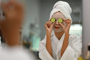 年轻的女人面部面具脸持有片新鲜的黄瓜采取水疗中心护肤品程序首页