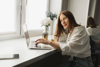 关闭年轻的漂亮的<strong>女人喝茶</strong>打破打字浏览在线移动PC工作电脑坐着舒适的房间距离学习工作打破咖啡时间概念