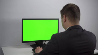 年轻的商人坐着前面电脑绿色屏幕男人。西装作品屏幕浓度关键