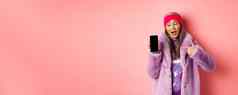 在线购物时尚概念很酷的亚洲奶奶时尚的人造皮毛外套指出手指左空白智能手机屏幕检查互联网促销粉红色的背景