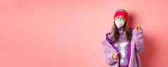 冠状病毒购物概念时髦的上了年纪的亚洲女人呼吸器闪闪发光的闪亮的衣服指出上角落里怀疑粉红色的背景
