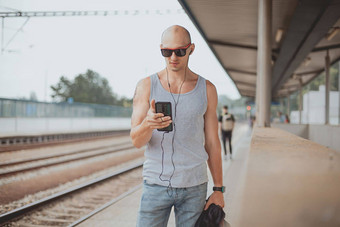 年轻的男人。t恤平台等待火车移动电话男人。火车站平台郊区袋移动电话旅行火车