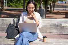 年轻的亚洲女人会说话的视频闲谈，聊天移动PC坐着板凳上在线会议远程