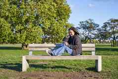 年轻的女人坐着板凳上公园移动电话屏幕发短信发送消息应用程序闲谈，聊天