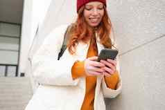 红色头发的人女孩年轻的女人旅游背包持有智能手机路线移动应用程序搜索酒店电话地图微笑幸福的