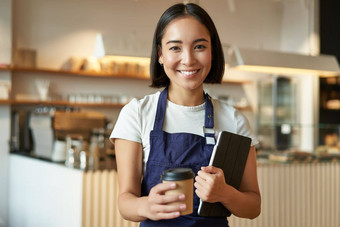 微笑咖啡师咖啡馆女服务员给<strong>外卖</strong>咖啡订单准备卡布奇诺咖啡<strong>外卖</strong>站蓝色的围裙平板电脑