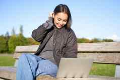 年轻的浅黑肤色的女人女孩坐在公园移动PC手表视频浏览互联网休息在户外板凳上阳光明媚的公园