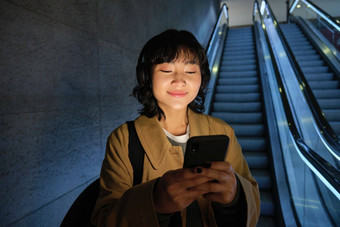 肖像快乐美丽的亚洲女孩站智能手机自动扶梯地铁站通勤管