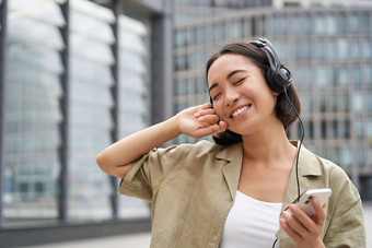 快乐年轻的女人跳舞街道听音乐耳机持有智能手机