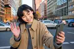 快乐亚洲女孩旅游需要自拍城市中心使视频调用波智能手机相机问候电话