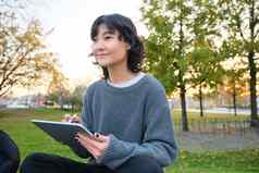 肖像年轻的微笑朝鲜文女孩图形设计师艺术家画数字平板电脑笔工具坐着公园新鲜的空气scatching采取笔记