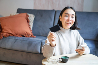 年轻的女人生活房间显示信贷卡智能手机支付订单在线购物应用程序