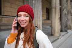 微笑红色头发的人女旅游会谈移动电话走城市快乐学生红色的他调用朋友站街智能手机