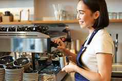 微笑年轻的亚洲咖啡师女孩咖啡机轮船热气腾腾的牛奶卡布奇诺咖啡订单站围裙工作咖啡馆