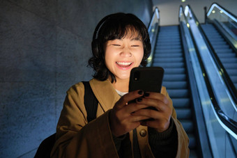 笑可爱的朝鲜文女孩自动扶梯管地下<strong>地铁</strong>移动<strong>电话</strong>看smth有趣的智能手机应用程序