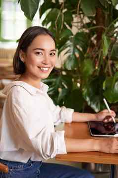 垂直拍摄年轻的亚洲女人数字平板电脑图形笔画抓坐着咖啡馆杯咖啡