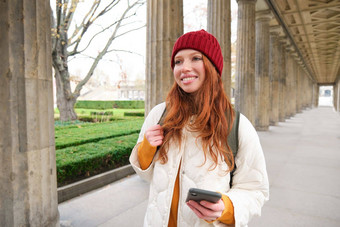 移动宽带人微笑红色头发的人女孩背包智能手机街持有移动电话应用程序